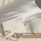 Silver gray satin pillowcase with gift box and matching scrunchie on beige bedding.