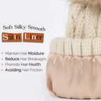 Cream knit winter beanie with beige satin lining and faux fur pompom, text highlighting satin liner benefits.